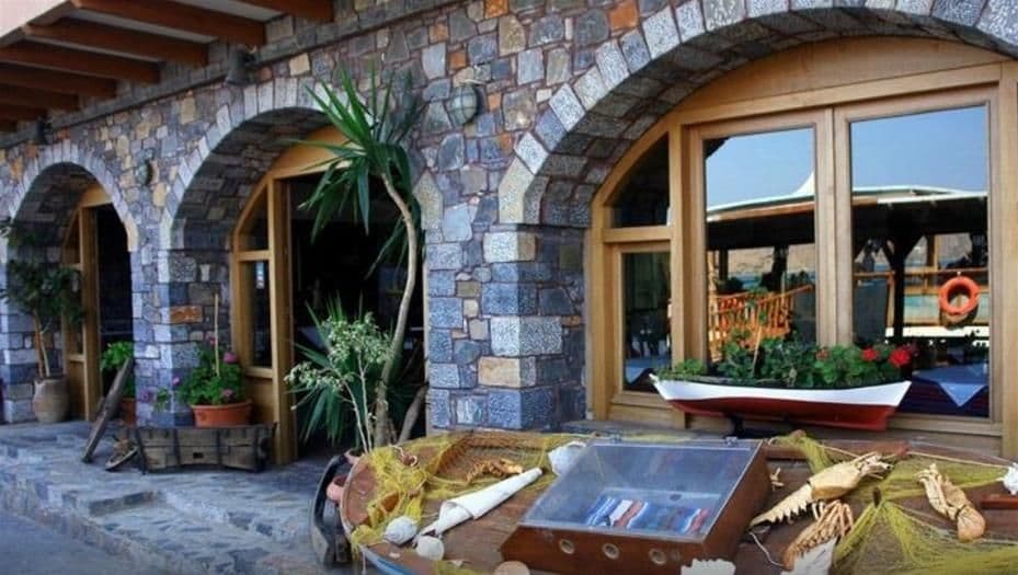 A stone building with arched doorways and windows, a boat outside, and various plants and items on the ground.