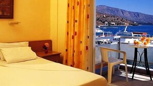 A hotel room with a bed, a small table with a chair, and a view of the sea and boats. - Aristea Hotel (Agios Nikolaos)