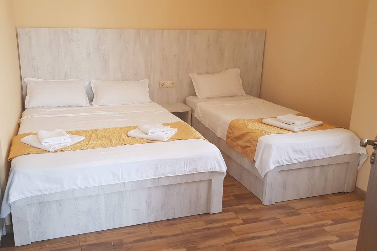A hotel room with two beds, each with white bedding and a wooden headboard. There are towels on the beds and a wooden floor.