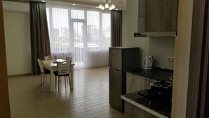 Moderni keittiö, jossa on jääkaappi, vedenkeitin ja liesi. Keittiössä on myös ruokailutila, jossa on pöytä ja tuolit.