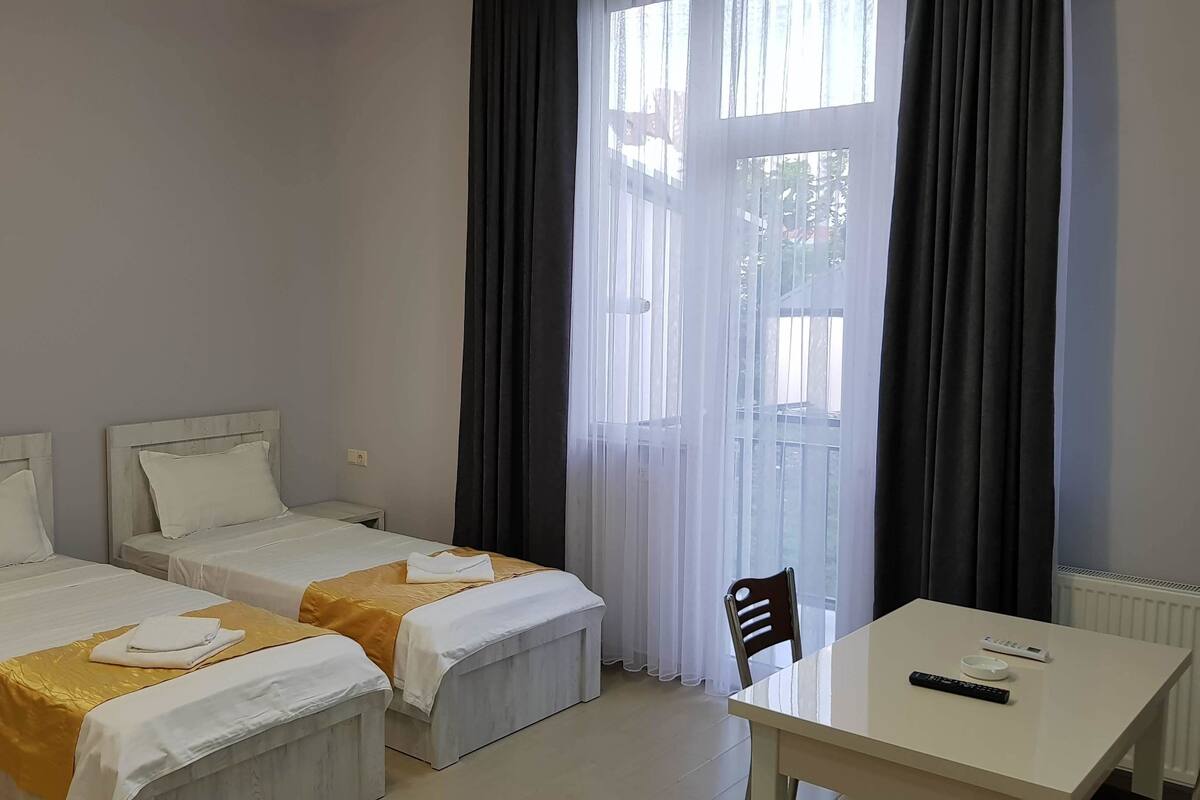 A hotel room with two single beds, a small table, and a chair.