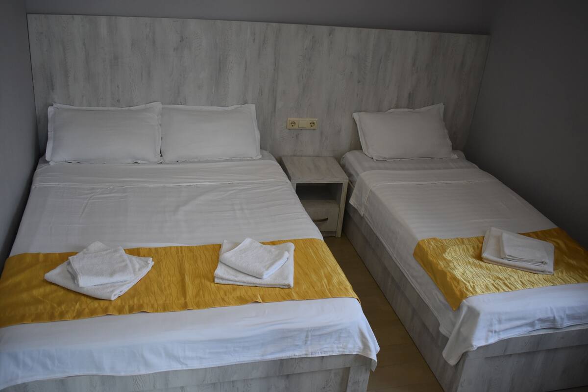 A hotel room with two single beds, each with white linens and a yellow accent.