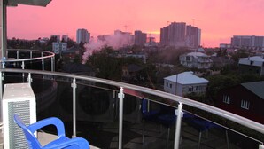 Parveke, jolta avautuu näkymä kaupunkimaisemaan auringonlaskun aikaan. Näkymässä on asuintaloja ja rakennustyömaalla oleva nosturi.
