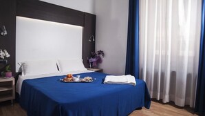 Ein Hotelzimmer mit einem großen Bett, einem Nachttisch mit Lampe und einem Fenster mit Vorhängen.