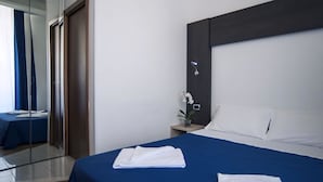 Ein Hotelzimmer mit einem großen Bett, einem Nachttisch mit Lampe, einem Spiegel und Blick auf einen blauen Vorhang sowie ein weiteres Zimmer.