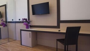 Ein Zimmer mit Schreibtisch, Stuhl, kleiner Kommode, Wandfernseher und Spiegel.