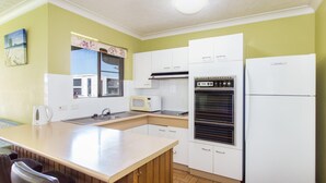 Een kleine keuken met witte kasten, een magnetron, een oven en een koelkast.