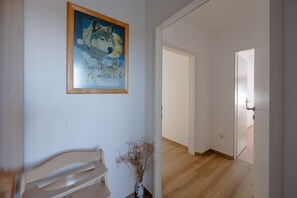 Un corridoio con pavimento in legno, un quadro appeso al muro e un vaso con piante essiccate.