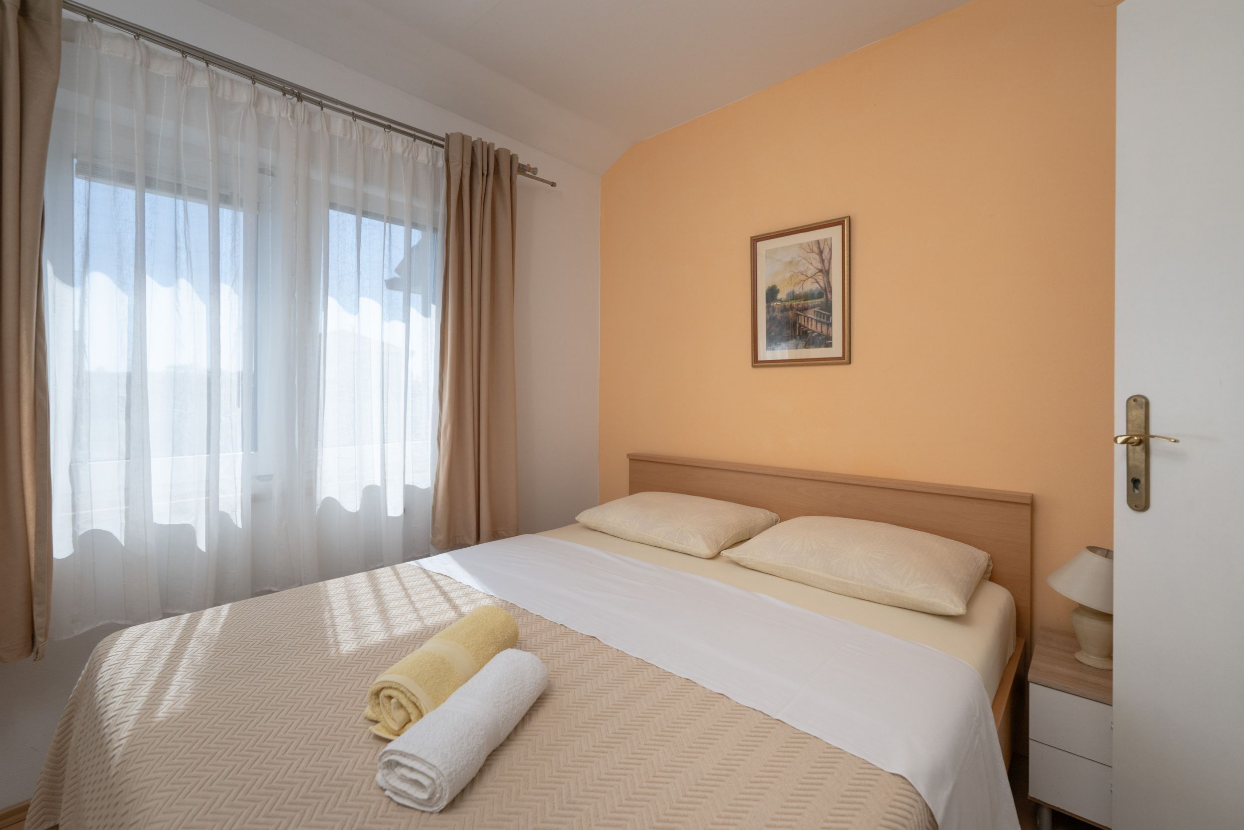 A hotel room with a bed, a painting on the wall, and a window with curtains.