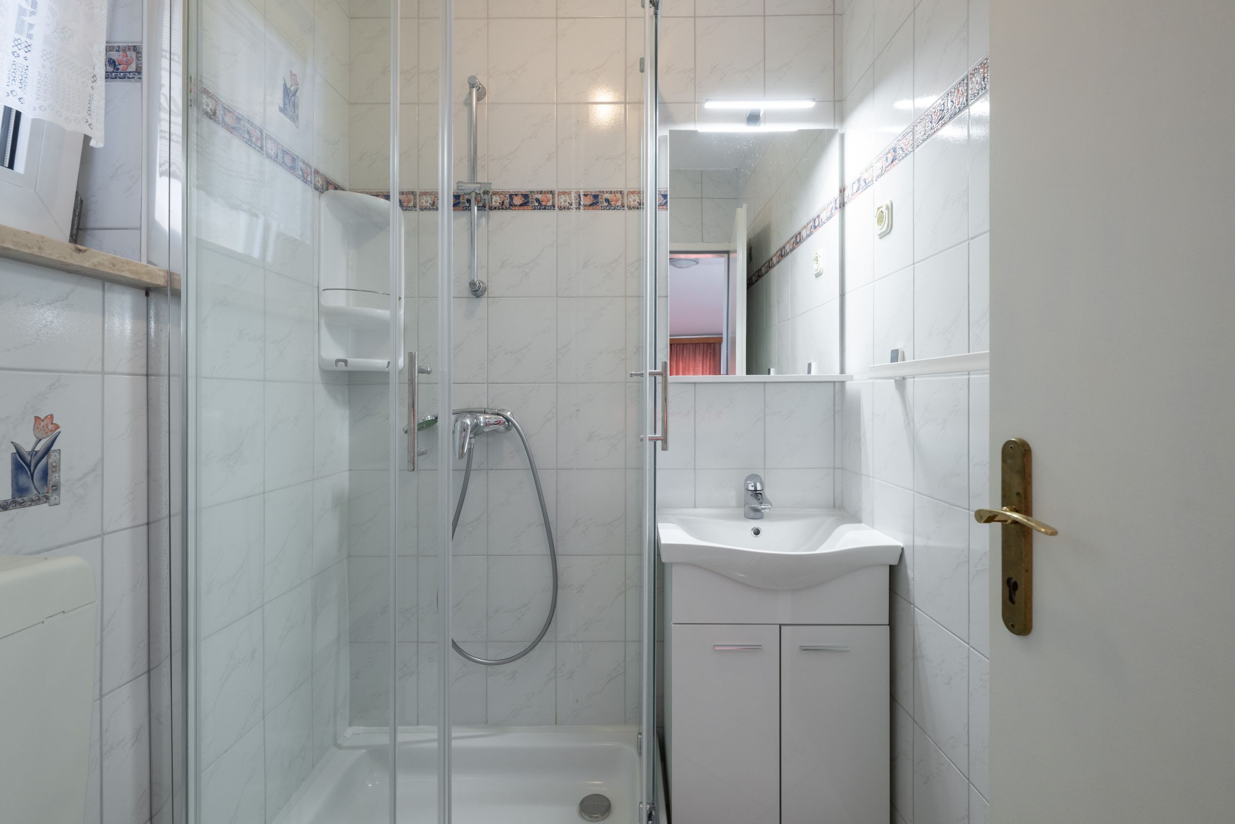 A bathroom with a glass-enclosed shower, a sink, and a mirror.