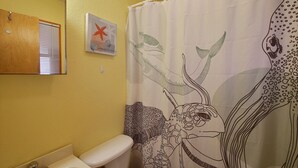 Bagno con parete gialla, vasca da bagno bianca, WC bianco e tenda da doccia con motivi marini.