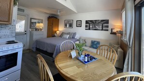 A compact room with a bed, a dining table, a kitchenette, and a view of the outdoors.