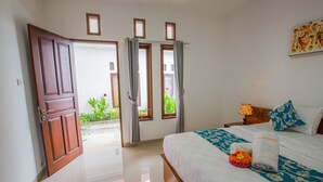 A hotel room with a bed, a nightstand, a lamp, and a view of the outside. - Arie Guest House Nusa Penida (Penida Island)