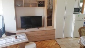 A living room with a flat-screen TV, wooden cabinet, and a dining area with a table. - Studio apartment in Vir with Balcony, Air condition, WIFI, Washing machine (4776-3) (Vir)