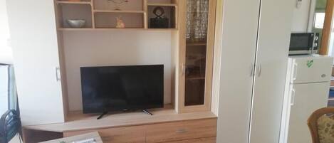A living room with a flat-screen TV, wooden cabinet, and a dining area with a table.