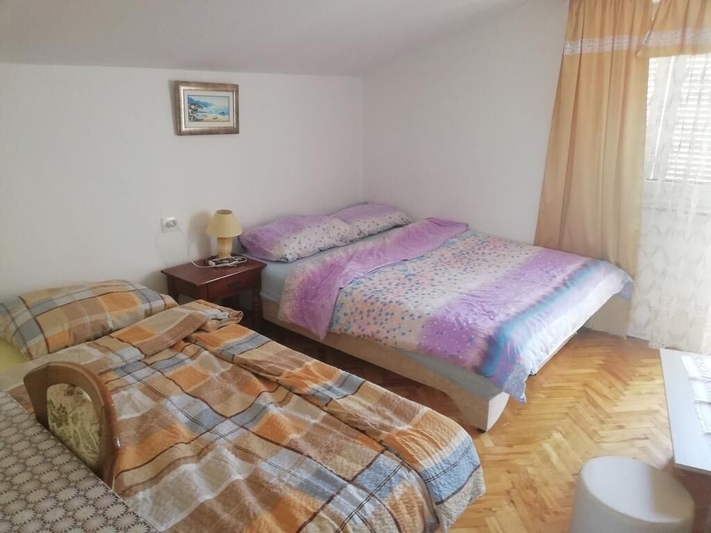 A bedroom with two beds, a nightstand, a lamp, a picture on the wall, and a window with curtains.