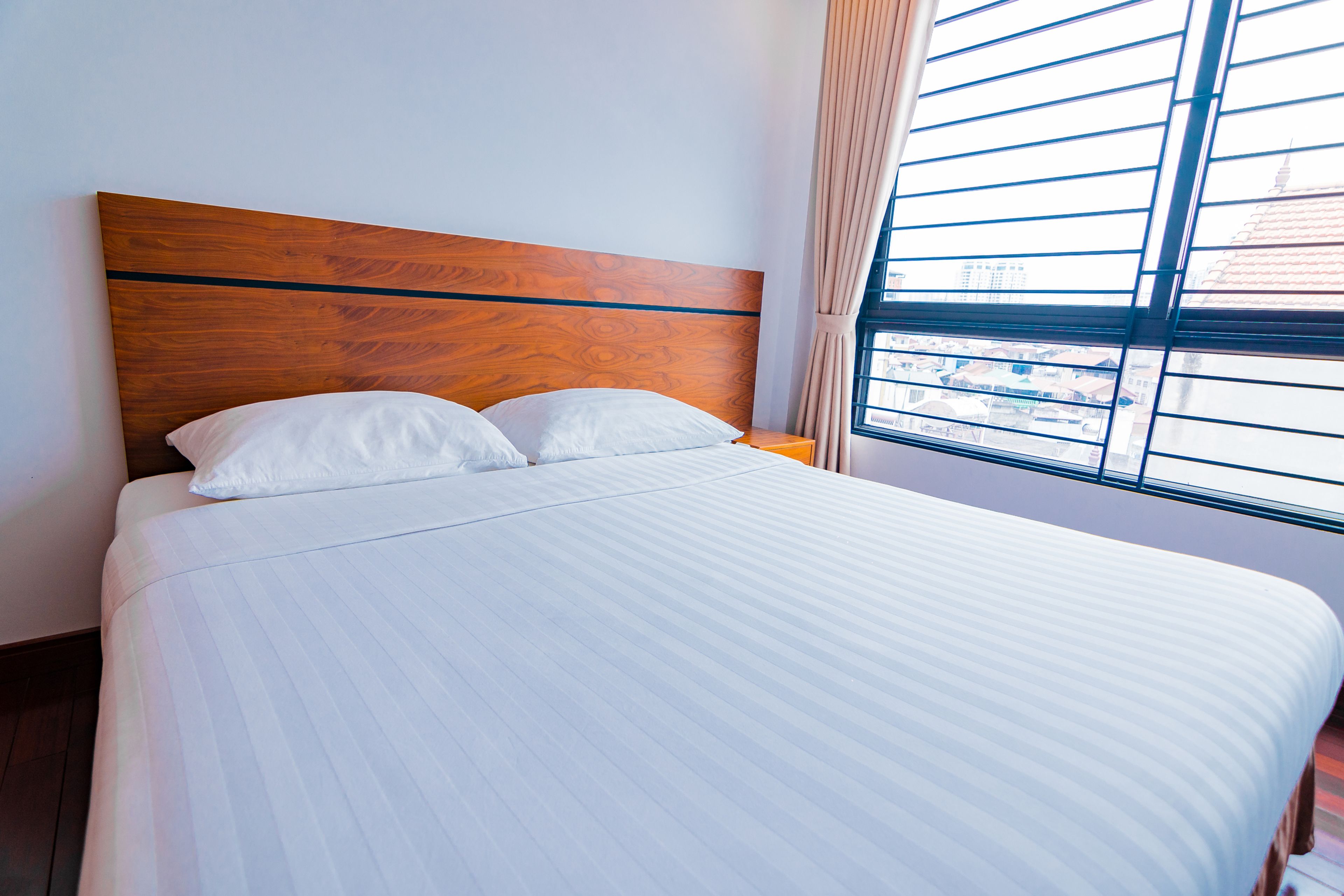 A neatly made bed with a wooden headboard, white bedding, and a window with blinds.