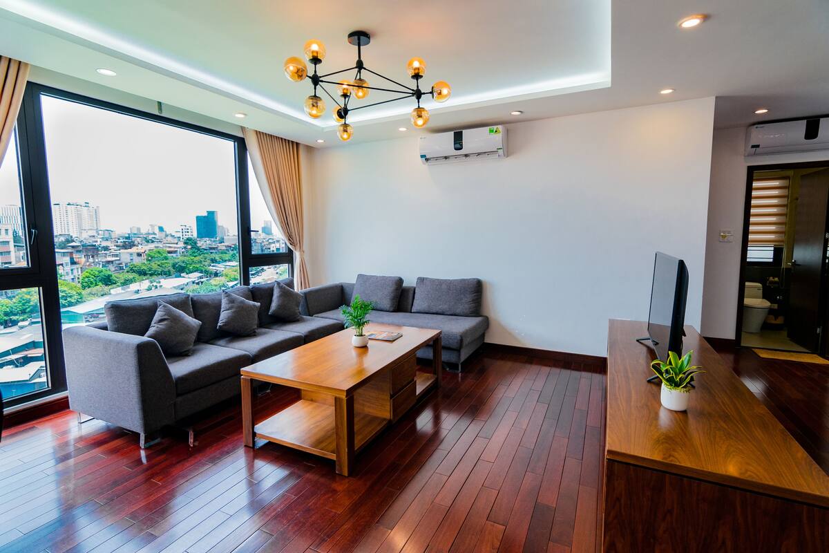 A modern living room with a large sofa, a wooden coffee table, and a TV on a wooden stand.