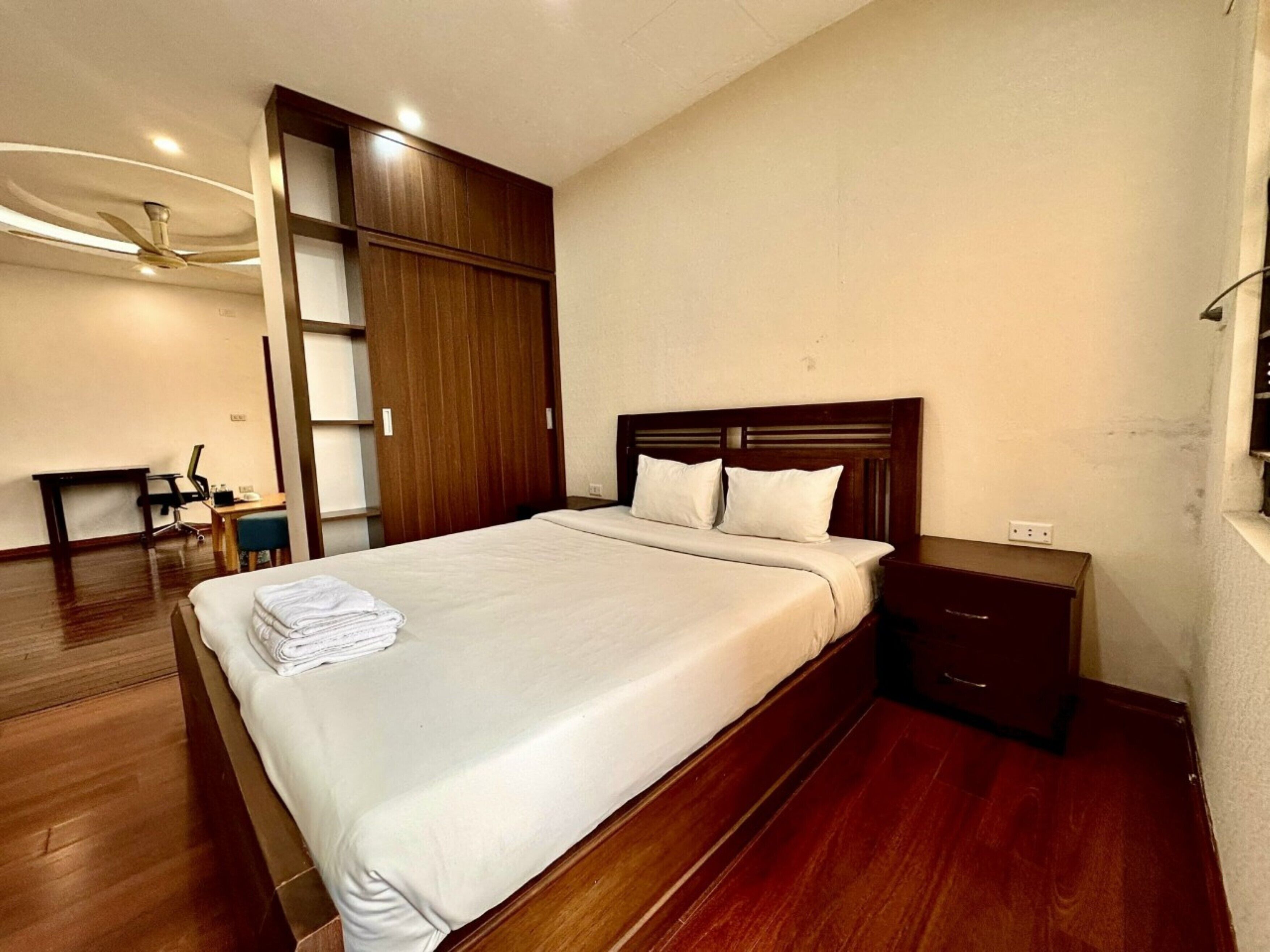 A bedroom with a large bed, wooden headboard, a desk, and a wardrobe.