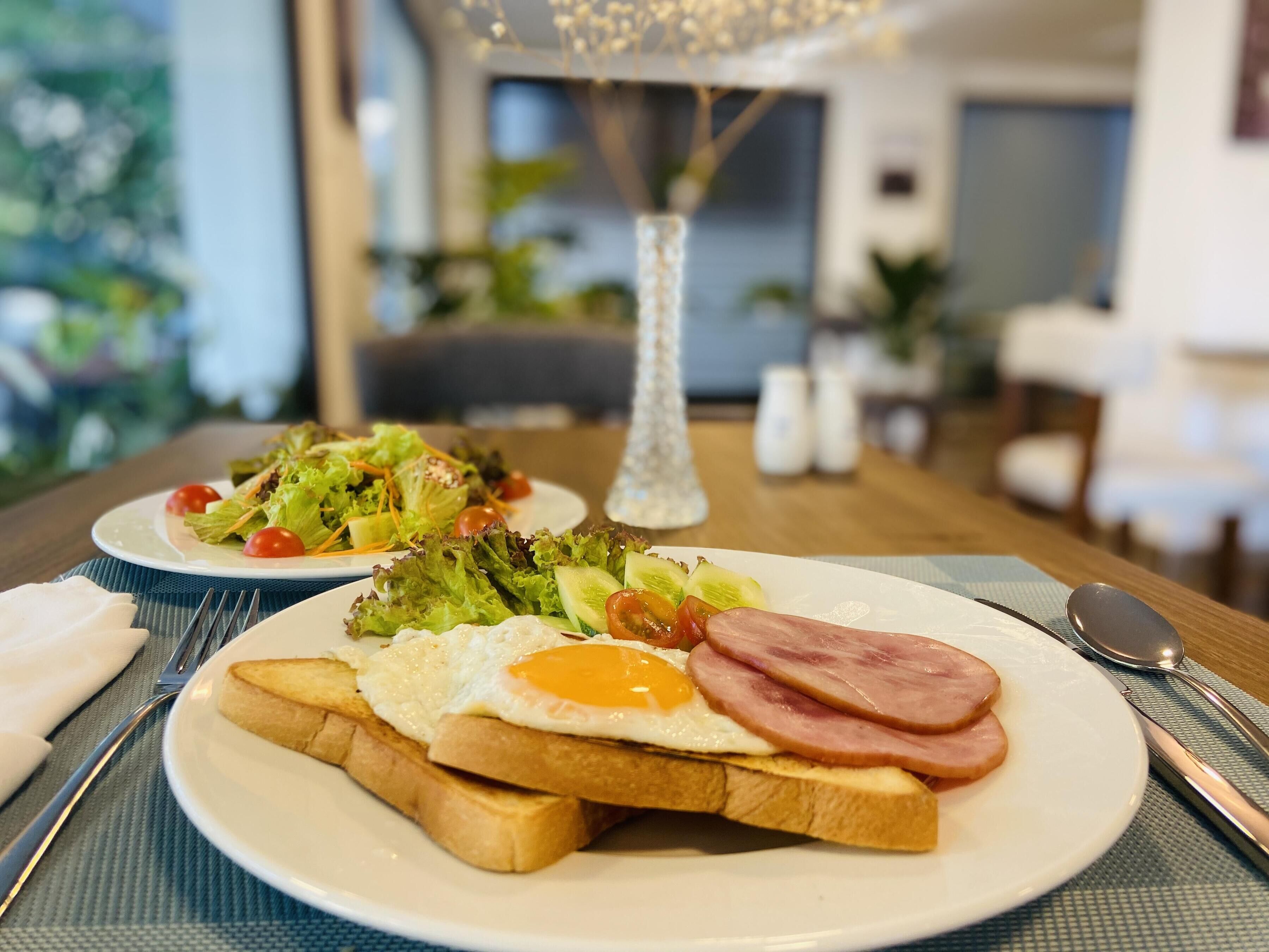 A breakfast setting with two plates, one with toast, egg, and ham, and another with a salad.
