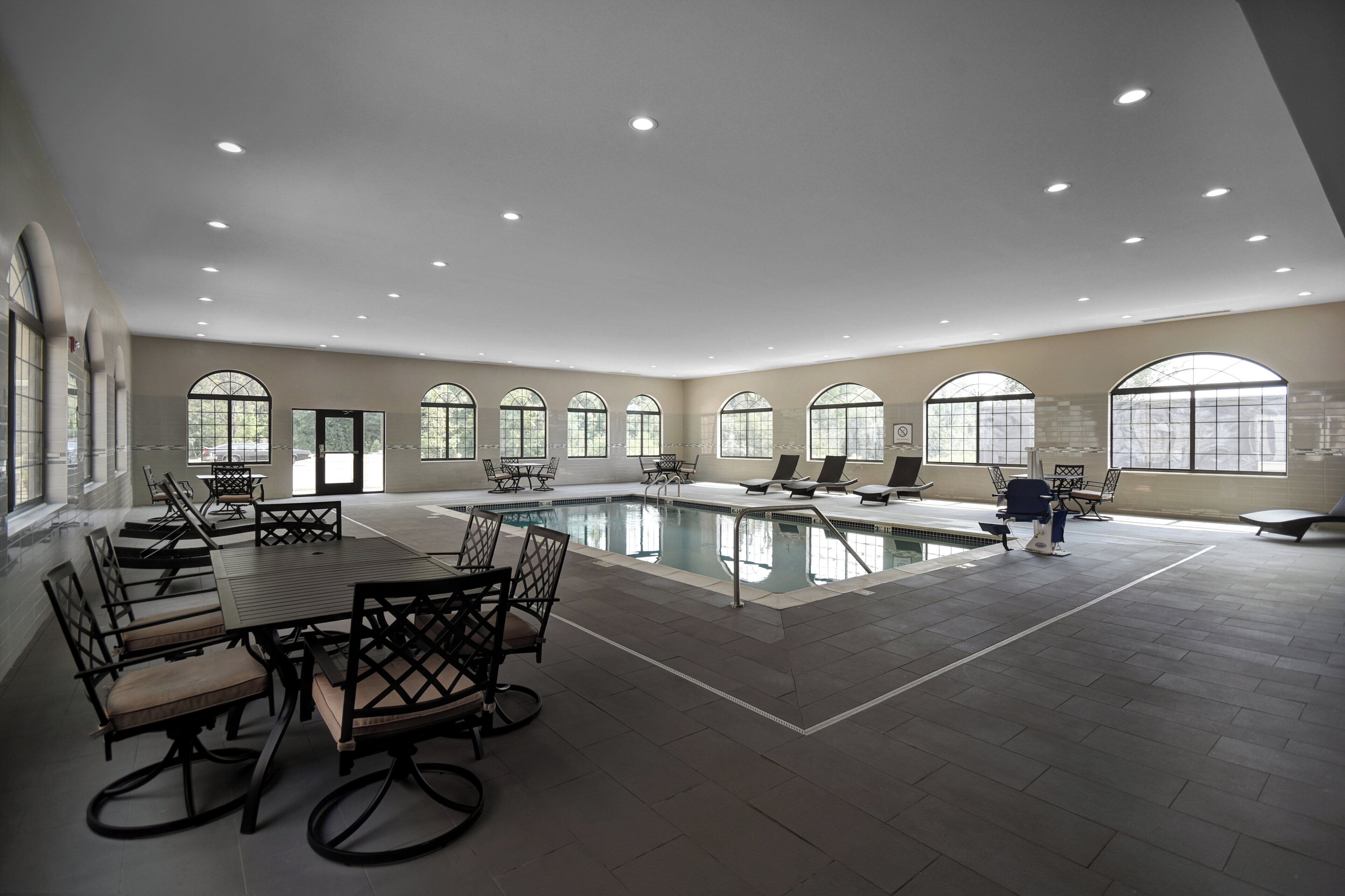 A spacious indoor swimming pool area with multiple seating arrangements and large windows.