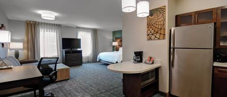 Una habitación de hotel con kitchenette, cama, escritorio y televisor.