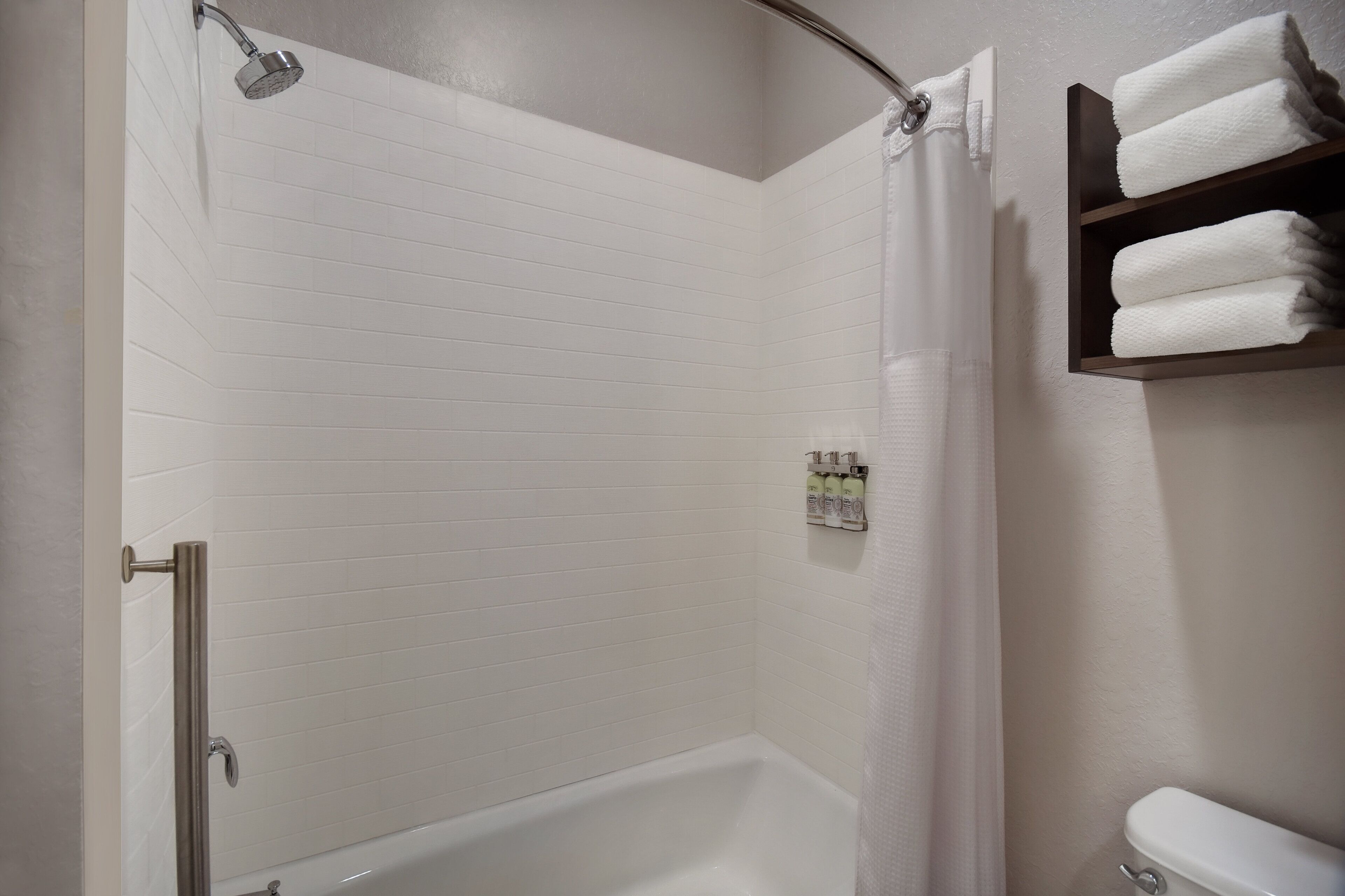 A modern bathroom with a white tiled shower, a glass door, and a shelf with folded towels.