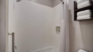 A modern bathroom with a white tiled shower, a glass door, and a shelf with folded towels.