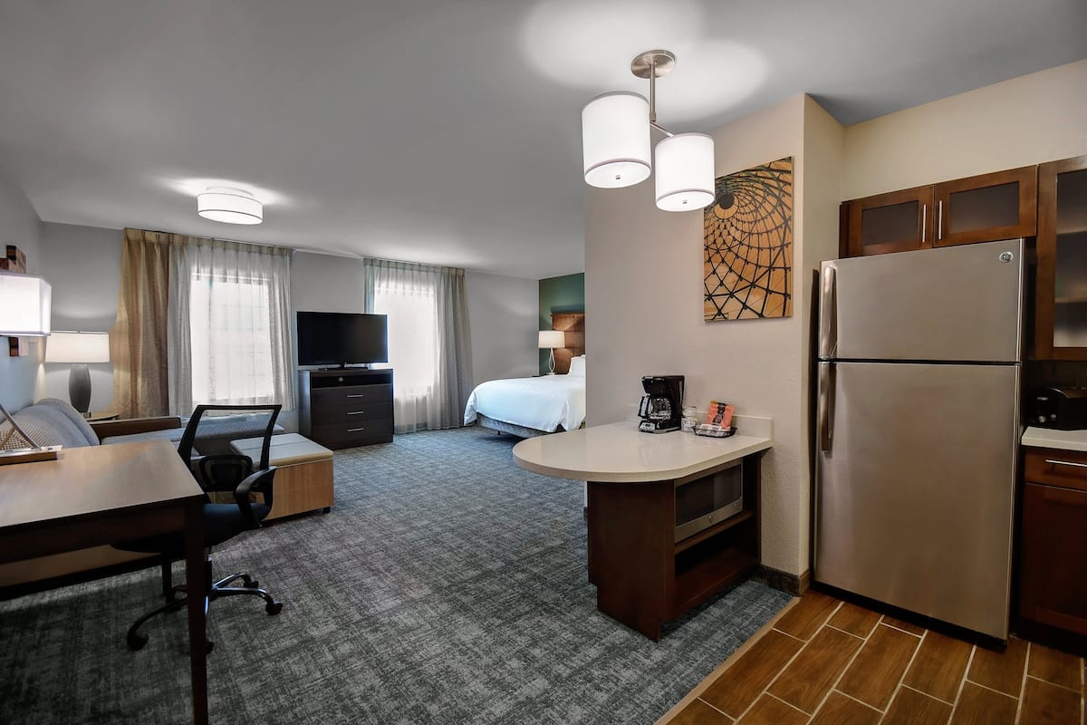 A hotel room with a kitchenette, a bed, a desk, and a TV.