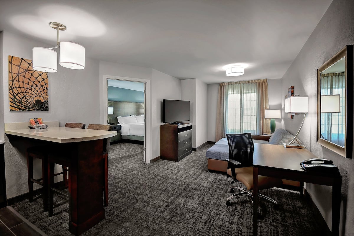 A hotel room with a dining area, a bed, a TV, a desk, and a lamp.
