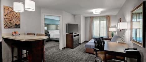 Habitación de hotel con comedor, cama, televisión, escritorio y lámpara.