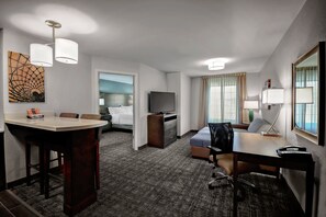 A hotel room with a dining area, a bed, a TV, a desk, and a lamp.