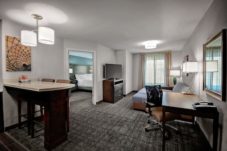A hotel room with a dining area, a bed, a TV, a desk, and a lamp.