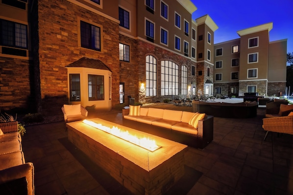 Un patio con una chimenea, mobiliario exterior y un edificio con múltiples ventanas y balcones.