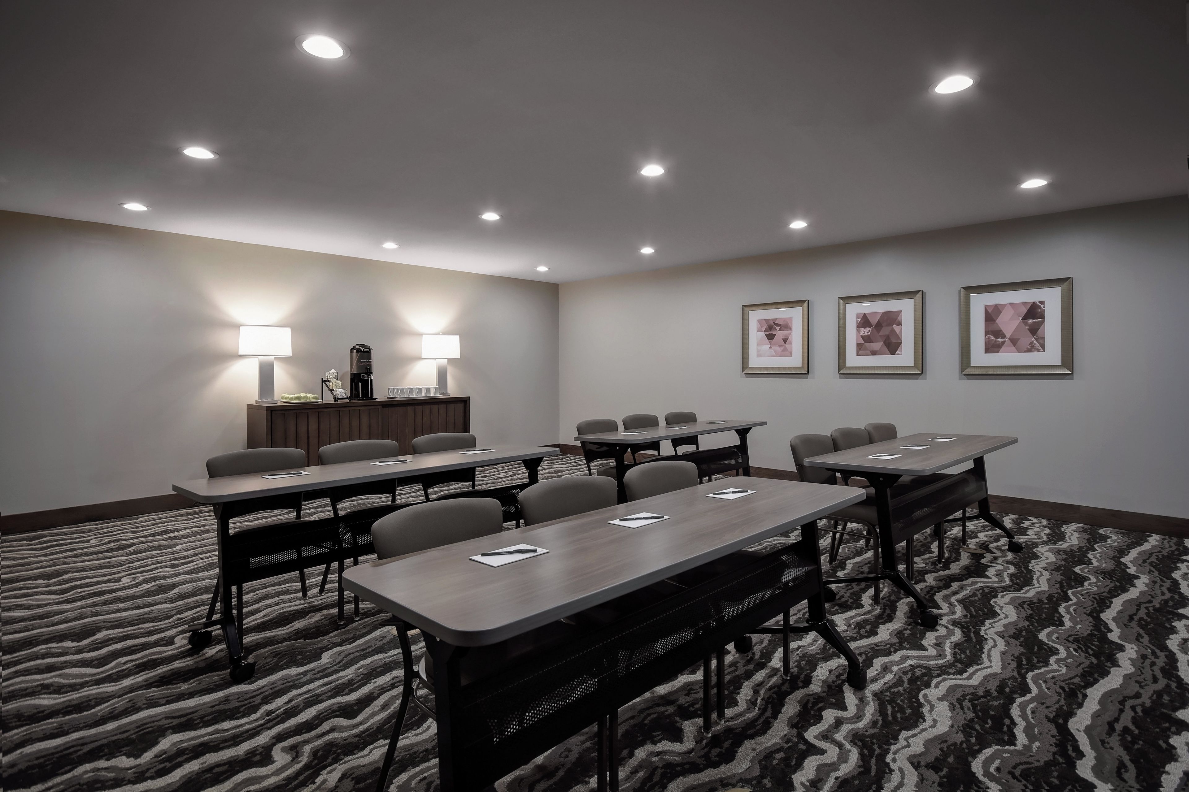 A conference room with tables, chairs, a reception desk, and three framed pictures on the wall.