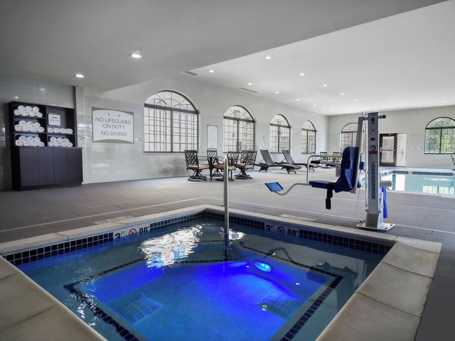 A swimming pool with a lifeguard sign, lounge chairs, and a tiled wall with towels.