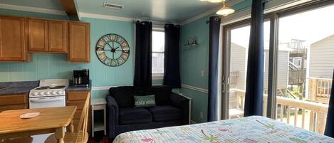 A cozy room with a bed, a dining table with chairs, a kitchen area with a stove, and a large window.