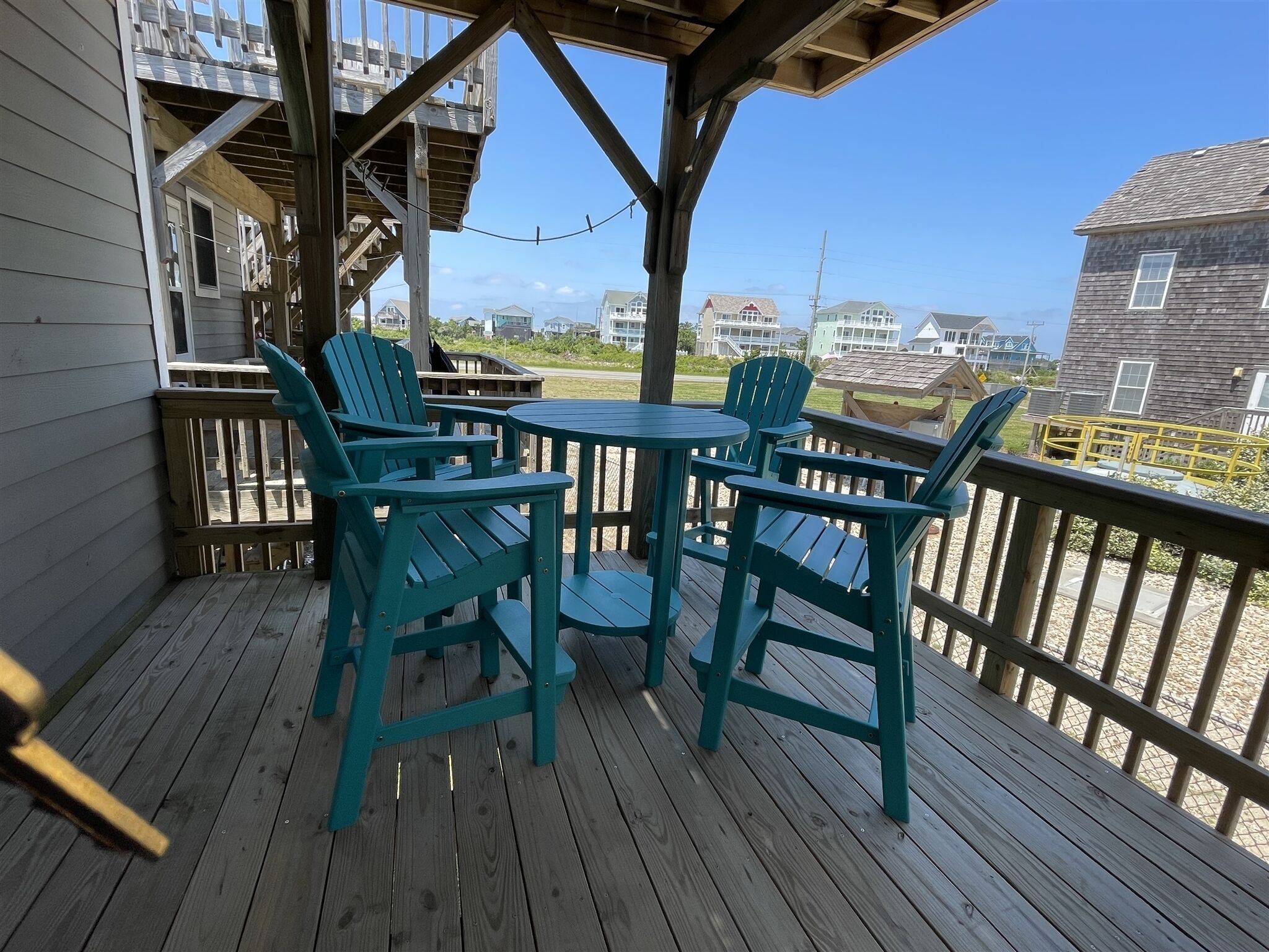 A wooden deck with two green Adirondack chairs and a small round table.
