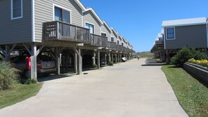 Une rangée de maisons à deux étages, dotées de balcons, un trottoir en béton et un ciel d’un bleu limpide.