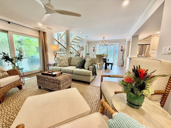 A spacious living room with a sofa, ottoman, and a dining area with a table and chairs. A staircase is visible leading to an upper level.