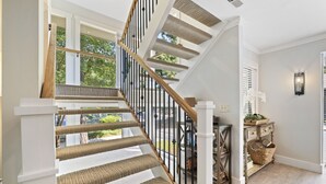 A staircase with a wooden handrail and white steps, leading to a landing area with a basket and a small table. - Island Song Villa - Newly Renovated, Pool, Tennis & Pickleball, Prime Location (Hilton Head Island,)