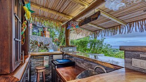 Una zona de bar con mostrador de piedra, taburetes de madera y vista al océano.