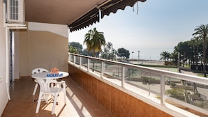 Un balcón con mesa y sillas, vista al mar y palmeras.