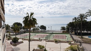 Complejo de canchas de tenis con varias canchas, rodeado de palmeras y vistas al mar.