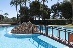 A swimming pool with a rock feature, surrounded by palm trees and a wooden deck. - FLORAZAR 2, VI-3-B (Cullera)