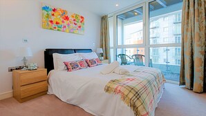 A bedroom with a large bed, a nightstand, a dresser, a window with curtains, and a colorful painting on the wall. - A modern apartment, equipped with everything for a comfortable stay (Portsmouth)