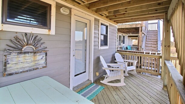 A wooden deck with a rocking chair and a table, a window, and a door.