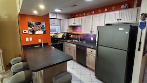 Uma cozinha com ilha central, armários brancos, geladeira e micro-ondas.
