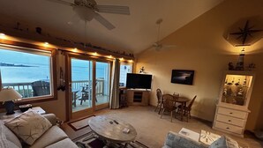 Uma sala de estar com sofá, poltronas, mesa de centro, televisão e varanda com vista para o mar.