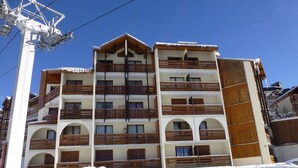 A multi-story hotel with balconies, a ski lift in the background, and snow on the ground. - Cozy Duplex for 5, Close to Ski Lifts & Shops, South-Facing Balcony – Alpe d'Huez (Huez)